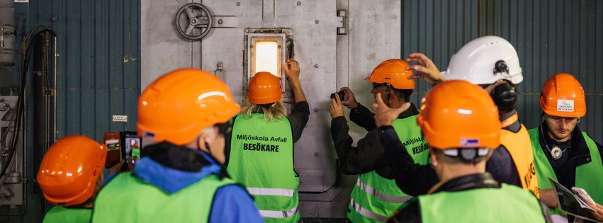 Fler personer med varselväst och skyddshjälm kollar in genom ett fönster till förbränningsugn.